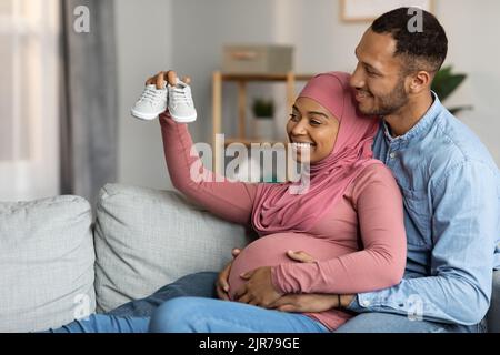 Happy Pregnant Black Muslim Couple Holding Tiny Baby Shoes And Smiling Stock Photo