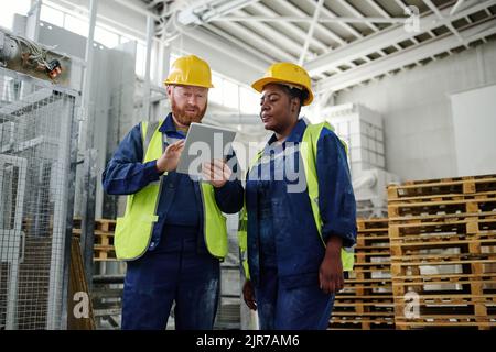 Young confident male engineer with tablet making presentation of new technical project to African American female colleague at meeting Stock Photo