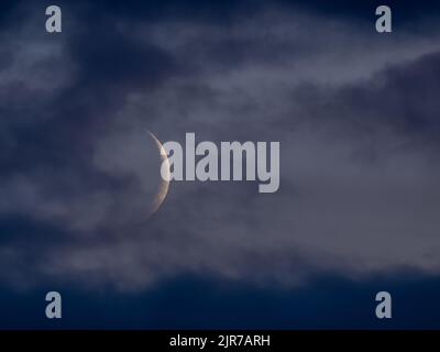 Waxing crescent Moon through light grey cloud Stock Photo