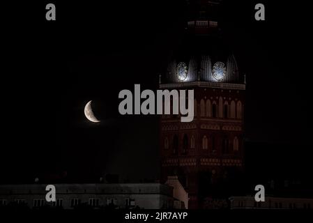 Beautiful quarter moon over Riga old town behind Domes cathedral clock. Stock Photo