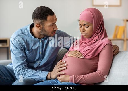 Caring Husband Comforting His Pregnant Black Muslim Wife Feeling Unwell At Home Stock Photo