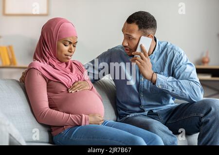 Worried Man Calling Doctor While His Pregnant Muslim Wife Suffering Prenatal Contractions Stock Photo