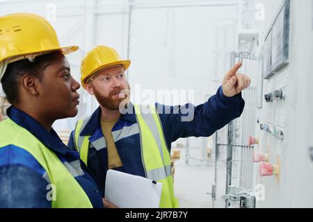 Confident technician or manager explaining female colleague how to start machine while pointing at control panel with buttons Stock Photo