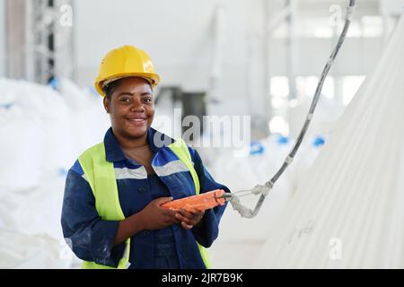Happy young female engineer of factory using switch remote control while lifting huge white heavy sacks and looking at camera Stock Photo