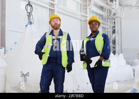 Two young confident colleagues in uniform and safety helmets having discussion of new industrial equipment and its quality Stock Photo