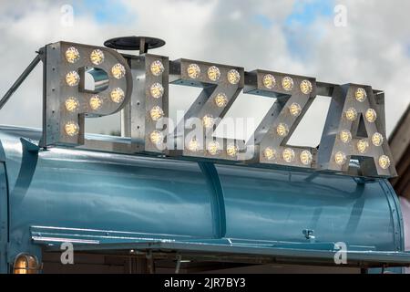 An LED illuminated Pizza sign on top of an outdoor food vendors stall. Stock Photo