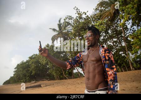 Young man vacationer looks at the sea and takes a selfie on the beach by the seaside. Stock Photo
