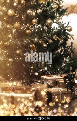 Beautifully decorated and illuminated Christmas tree with many presents under it in wooden rustic interior. Golden decoration and bokeh. Vintage toning. Stock Photo