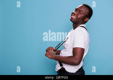 Handsome african ethnicity male model posing for camera while standing on blue background. Confident smiling heartily young man with vintage and attractive look. Studio shot Stock Photo