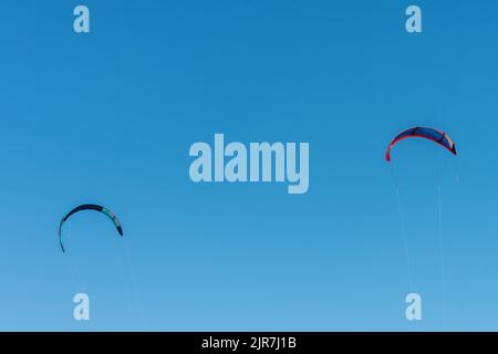 Two multicolored kitesurfing on blue sky background. Stock Photo