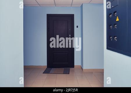 Dark brown door in the entrance of an apartment building with blue corridor walls Stock Photo