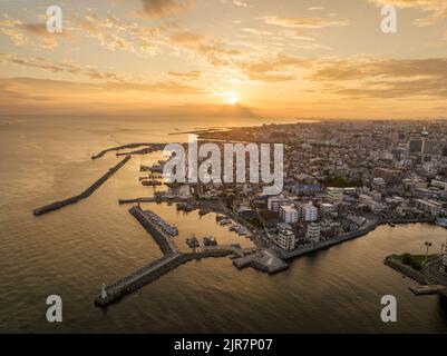 Aerial view of breakwaters at small harbor on coastal town at sunset Stock Photo