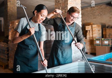 Cellar workers, making wine and mixing open tank with stirring, pressing and crushing tool for alcohol production. Happy staff and merchants in Stock Photo