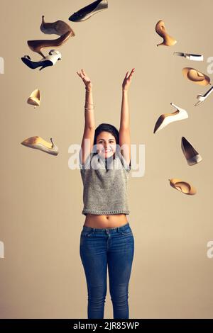 Love is in the air and it looks like shoes. Studio shot of a joyful young woman throwing a bunch of shoes in the air against a brown background. Stock Photo