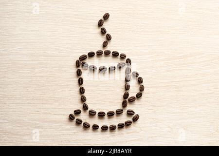 Coffee grains are laid out in the form of a cup. coffee bean close-up on a wooden table. Stock Photo