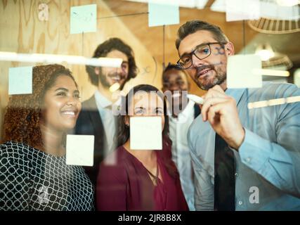 Putting the ideas into focus. coworkers using sticky notes on a glass wall during a meeting in the office. Stock Photo