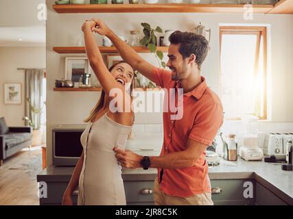 Joyful, dancing and loving couple bonding and having fun in the kitchen together at home. Energetic, fun and active relationship sharing a dance and Stock Photo