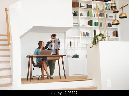 Putting their heads together at home. a happy young man checking in on his wife while she works from her desk at home. Stock Photo