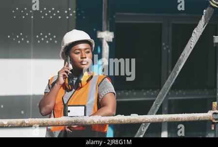 Construction worker talking on a phone call while standing in a building site. Professional builder discussing plans and strategy, checking the inside Stock Photo