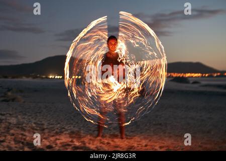 Add a little sparkle to your life. Portrait of a happy young man playing with a sparkler on the beach at sunset. Stock Photo
