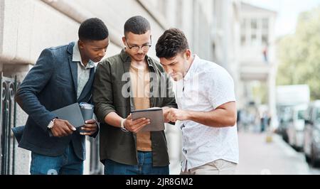 Team of creative designers checking a website for ux and ui while working for a startup. Group of young guys looking at a homepage on a tablet while Stock Photo