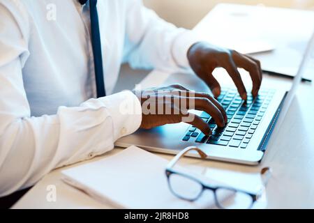 His typing game is on. Closeup of an unrecognizable man working and typing on his laptop at his desk with his reading glasses placed next to him in Stock Photo