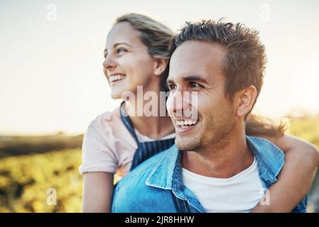 Looking fondly over their farm. a handsome young man piggybacking his girlfriend through the crops on their farm. Stock Photo