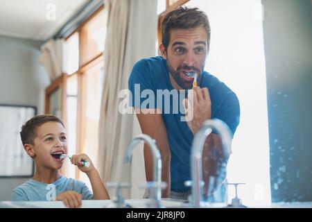 Make sure you get those teeth at the back. a handsome young man and his son brushing their teeth in the bathroom. Stock Photo