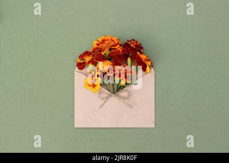 Orange flowers in craft envelope on green background. Top view Flat lay. Summer or autumn minimal greeting card. Stock Photo
