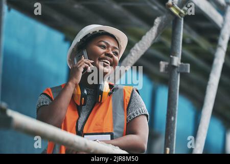 Construction manager, contractor and engineer talking on a phone while planning logistics at a building site in town. Happy, smiling and cheerful Stock Photo