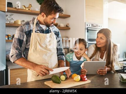 Knives are for grownups only, okay. two happy parents and their young daughter trying a new recipe in the kitchen together. Stock Photo