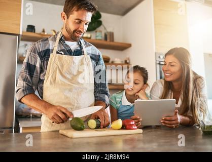 Let daddy show you how its done. two happy parents and their young daughter trying a new recipe in the kitchen together. Stock Photo