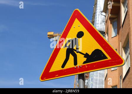 Genderless road work warning sign in front of a construction site. Stock Photo