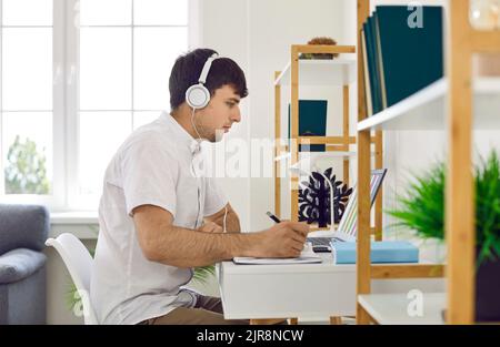 Young man in headphones studying or working online at his desk with laptop at home Stock Photo