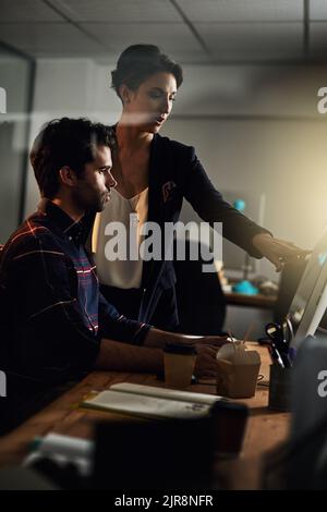 Putting in the extra hours to ensure their success. two colleagues working late on a computer in an office. Stock Photo