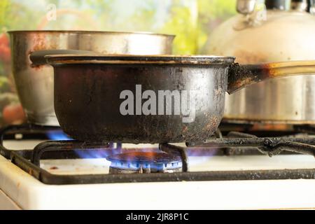 a dirty saucepan stands on a dirty gas stove in the kitchen at home, cooking soup on the stove, gas stove, kitchen Stock Photo