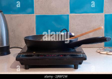 the frying pan is on a single induction electric stove on the kitchen table in the apartment, kitchen, frying pan on the stove Stock Photo