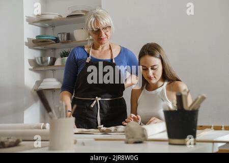 Pottery workshop in studio. People working with clay on the table. Adults learning to do ceramic plates. Pottery as hobby and leisure activity Stock Photo