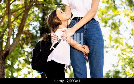 The daughter holds her mother's leg before leaving for school, she smiles at her and is happy. Stock Photo