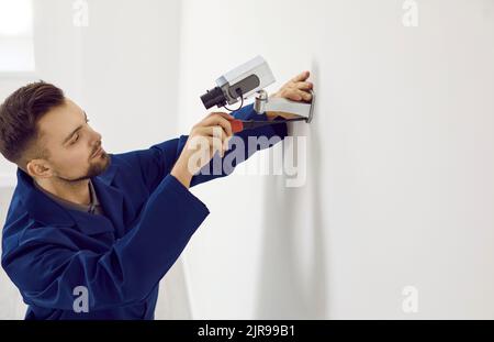 Male technician installs video surveillance camera on wall inside office for security. Stock Photo