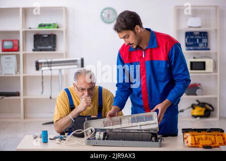 Two repairmen repairing air-conditioner at workshop Stock Photo