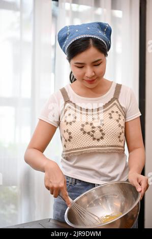 Portrait, Attractive young Asian female makes a homemade cupcake in her home kitchen, whisking her softened butter and sugar together in the mixing bo Stock Photo