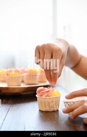 close-up image, A professional female baker making a cupcake in her house, decorating her fresh cupcake with sprinkles. Stock Photo