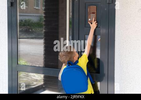 Caucasian boy confidently leaves home for his first day at preschool. A cute little boy with a school backpack rings the doorbell of the house. Stock Photo