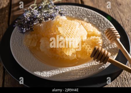 Honey and honeycombs on a white plate. Sweet food in a bowl on the table. A product of beekeeping. Lavender flower. Stock Photo