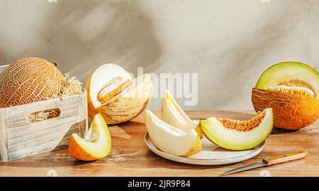 Various sliced melons on wooden table by stone wall Stock Photo