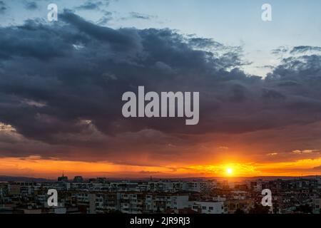 Sunset over multi-storey residential district. The setting sun low on the horizon while dark stormy cloud covering the blue sky. City residential area Stock Photo