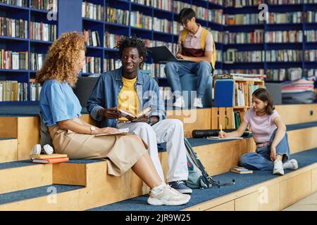 Diverse group of college students in library lounge, focus on black young man talking to friend Stock Photo