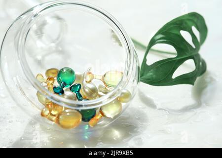 Serum capsules for healthy skin. Blurred background, glass jar with the capsules and green monstera leaf Stock Photo