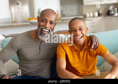 Portrait of happy african american male teenager with his father sitting on couch Stock Photo